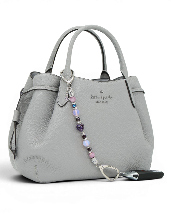 LD Keyfinder Orchid Flutter beaded accessory with lepidolite, opalite, and butterfly charm attached to a grey handbag.