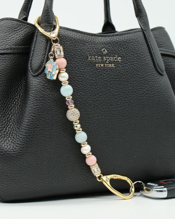 LD Keyfinder Pastel Garden charm with pink opal, pearls, aquamarine, and gold-plated beads on a black handbag.