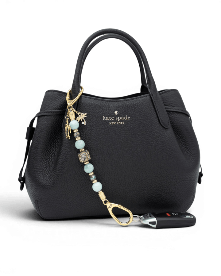 LD Keyfinder Paua Paradise beaded keychain with aqua jade, paua shell, and gold charms attached to a black handbag.