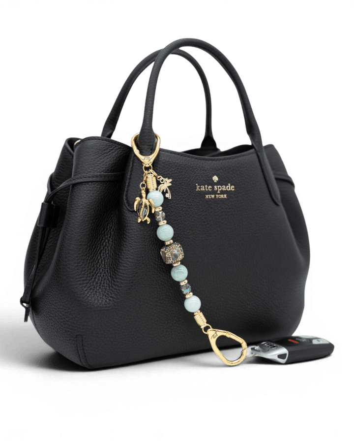 LD Keyfinder Paua Paradise beaded accessory with aqua jade, paua shell, and gold charms attached to a black handbag.