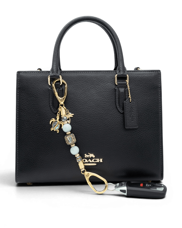LD Keyfinder Paua Paradise-Mini featuring aqua jade, paua shell, and gold charms attached to a black leather handbag.