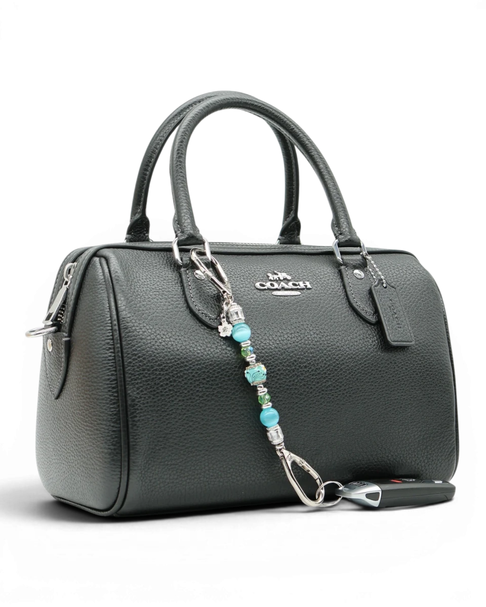 LD Keyfinder Petite Azure Meadow charm with aqua blue cat's eye beads, green glass beads, and a daisy charm attached to a black handbag.