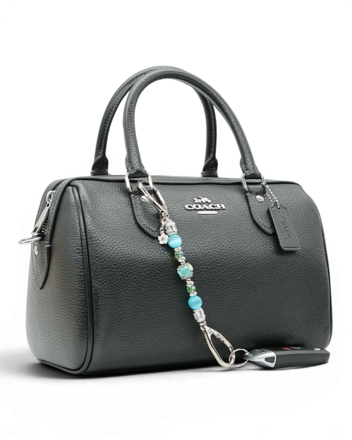 LD Keyfinder Petite Azure Meadow charm with aqua blue cat's eye beads, green glass beads, and a daisy charm attached to a black handbag.