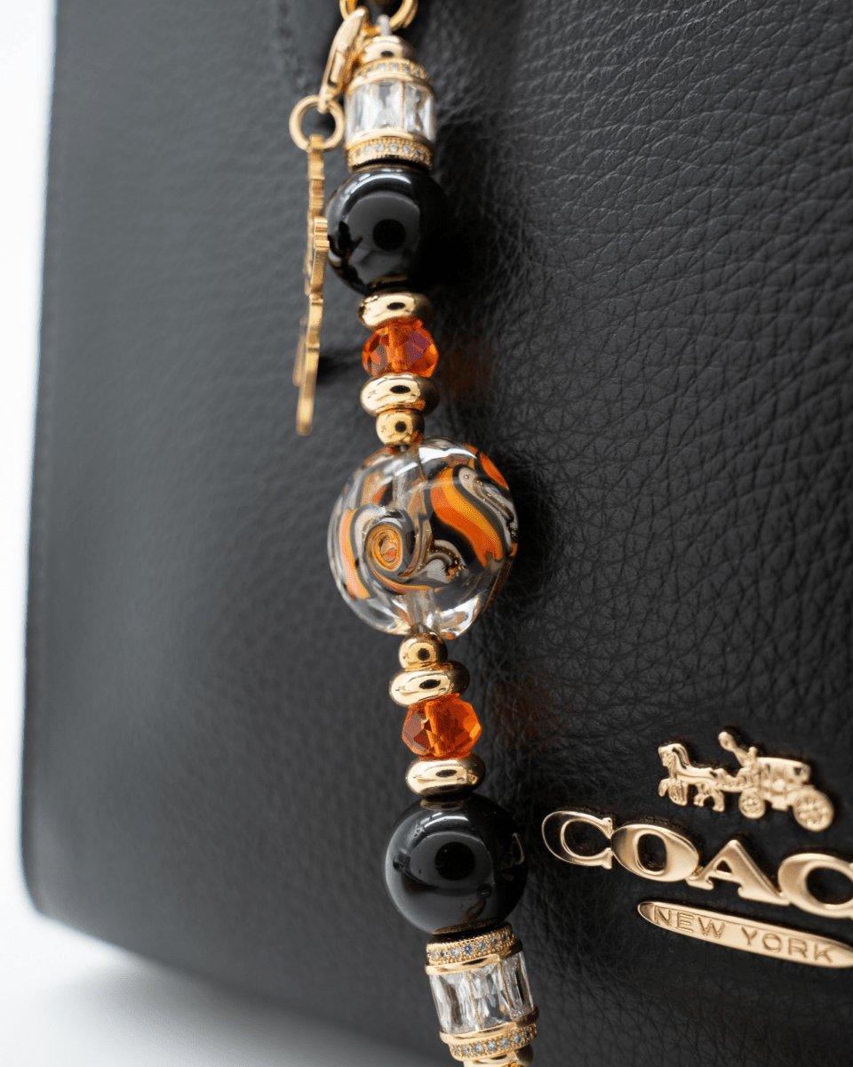LD Keyfinder Petite Bewitched Halloween accessory with obsidian, orange glass, and a gold witch charm on a black bag.