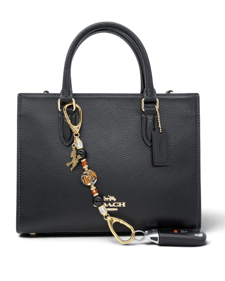 LD Keyfinder Petite Bewitched Halloween accessory with obsidian, orange glass, and a gold witch charm on a black bag.