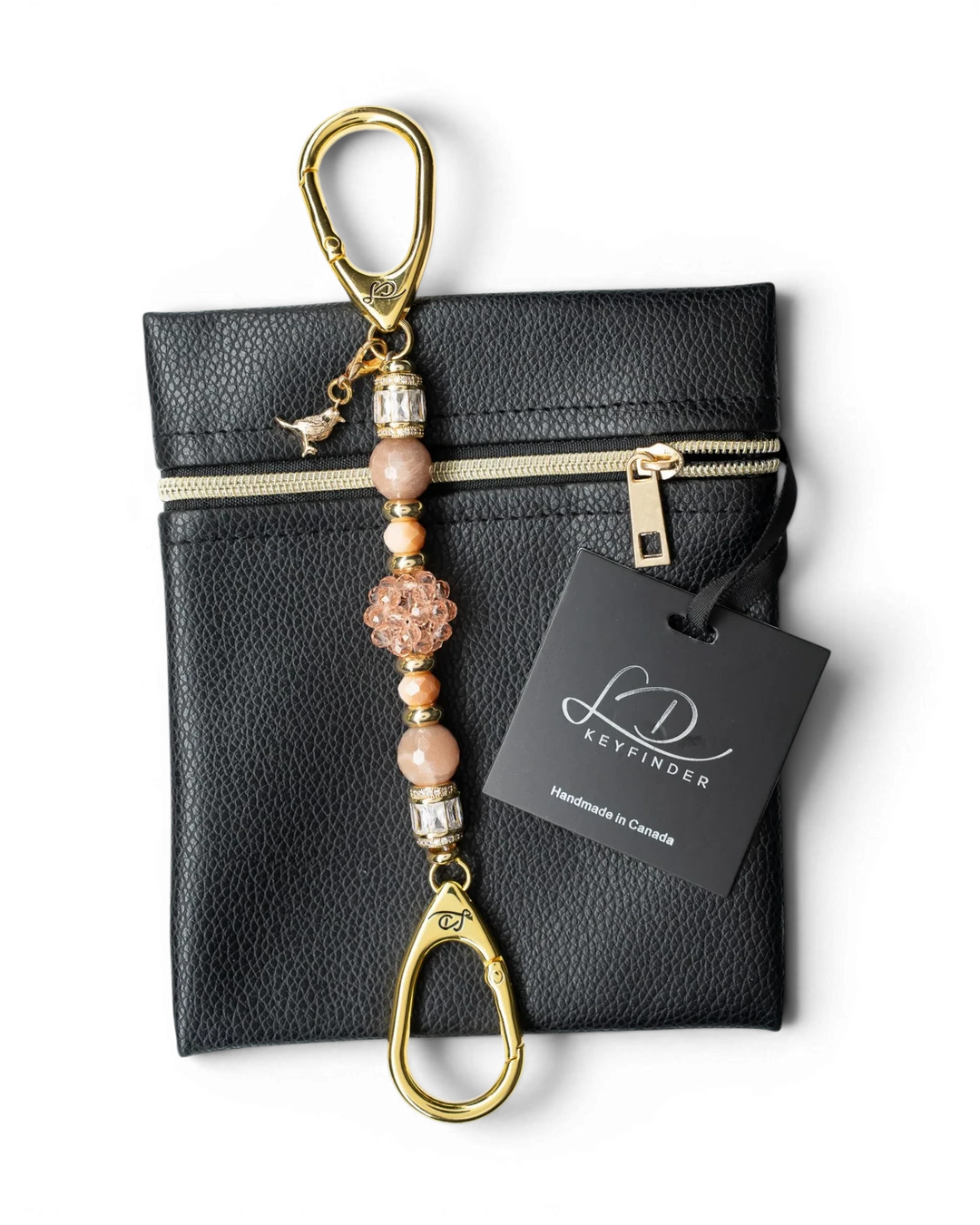 LD Keyfinder Petite Birdsong Bliss key chain with peach glass, sunstone beads, and gold bird charm on a black pouch.