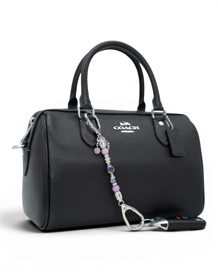 LD Keyfinder Petite Blooming Joy accessory with lavender Lepidolite and purple Jade beads attached to a black handbag.