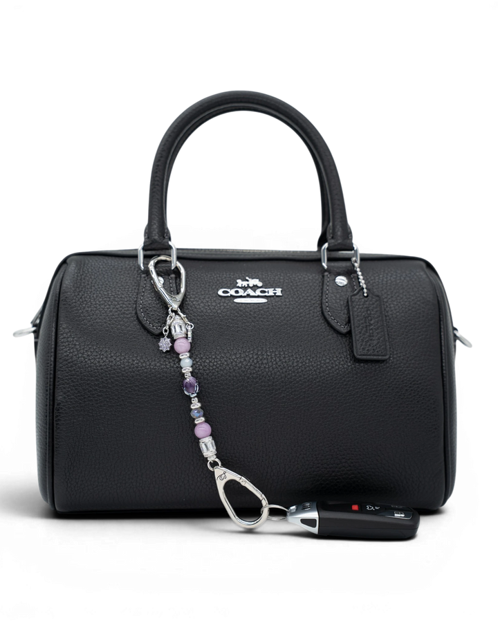 LD Keyfinder Petite Blooming Joy beaded accessory with lavender Lepidolite and purple Jade attached to a black handbag.