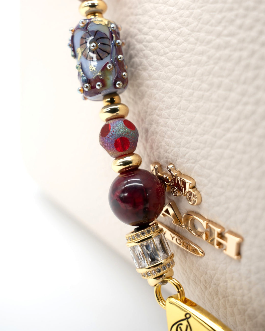 LD Keyfinder Petite Bordeaux Bloom featuring artisan glass, burgundy agate, and 18KT gold-plated accents on a handbag.
