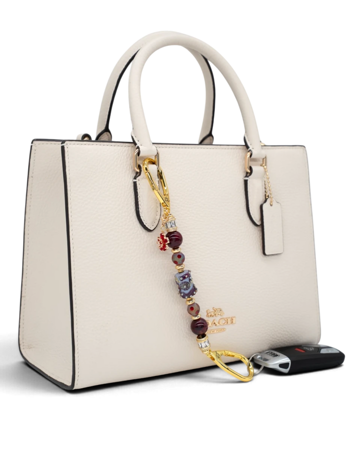LD Keyfinder Petite Bordeaux Bloom beaded keychain with burgundy agate and gold accents attached to a white handbag.