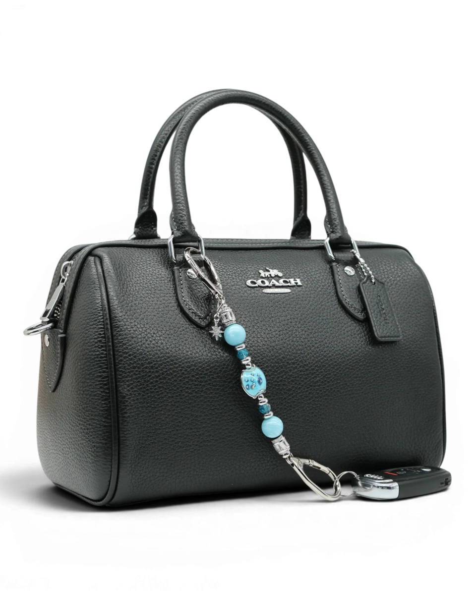 LD Keyfinder Petite Celestial Tide charm with turquoise, aqua, and silver beads, and a star charm, attached to a black handbag.
