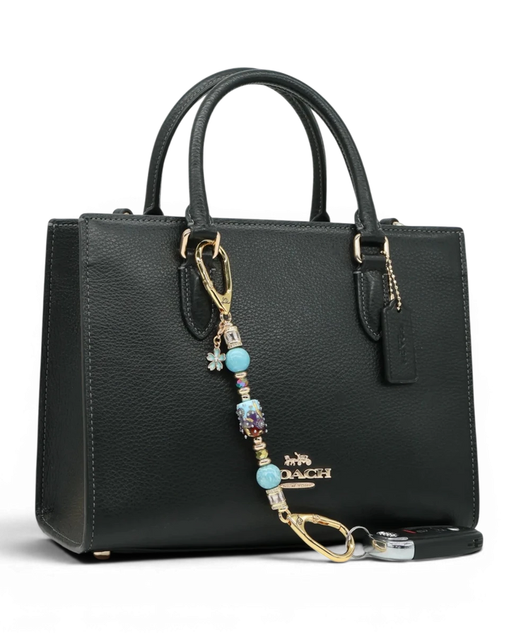 LD Keyfinder Petite Gilded Fantasy keychain with blue glass bead, gold leaf, larimar, and flower charm on black bag.