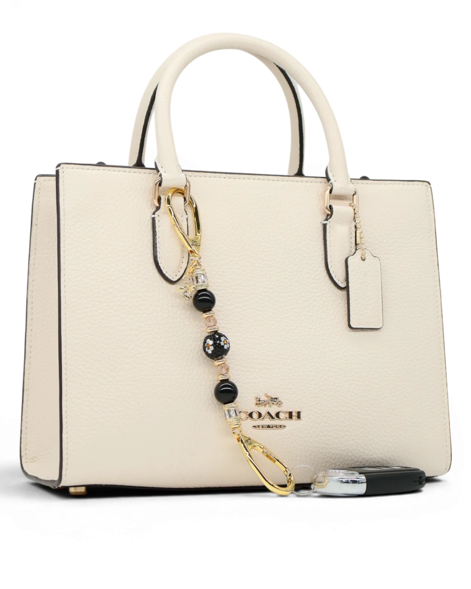 LD Keyfinder Petite Queen Bee II charm with black obsidian beads, crystals, and gold-plated accents on a cream handbag.