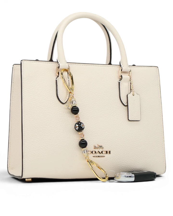 LD Keyfinder Petite Queen Bee II charm with black obsidian beads, crystals, and gold-plated accents on a cream handbag.