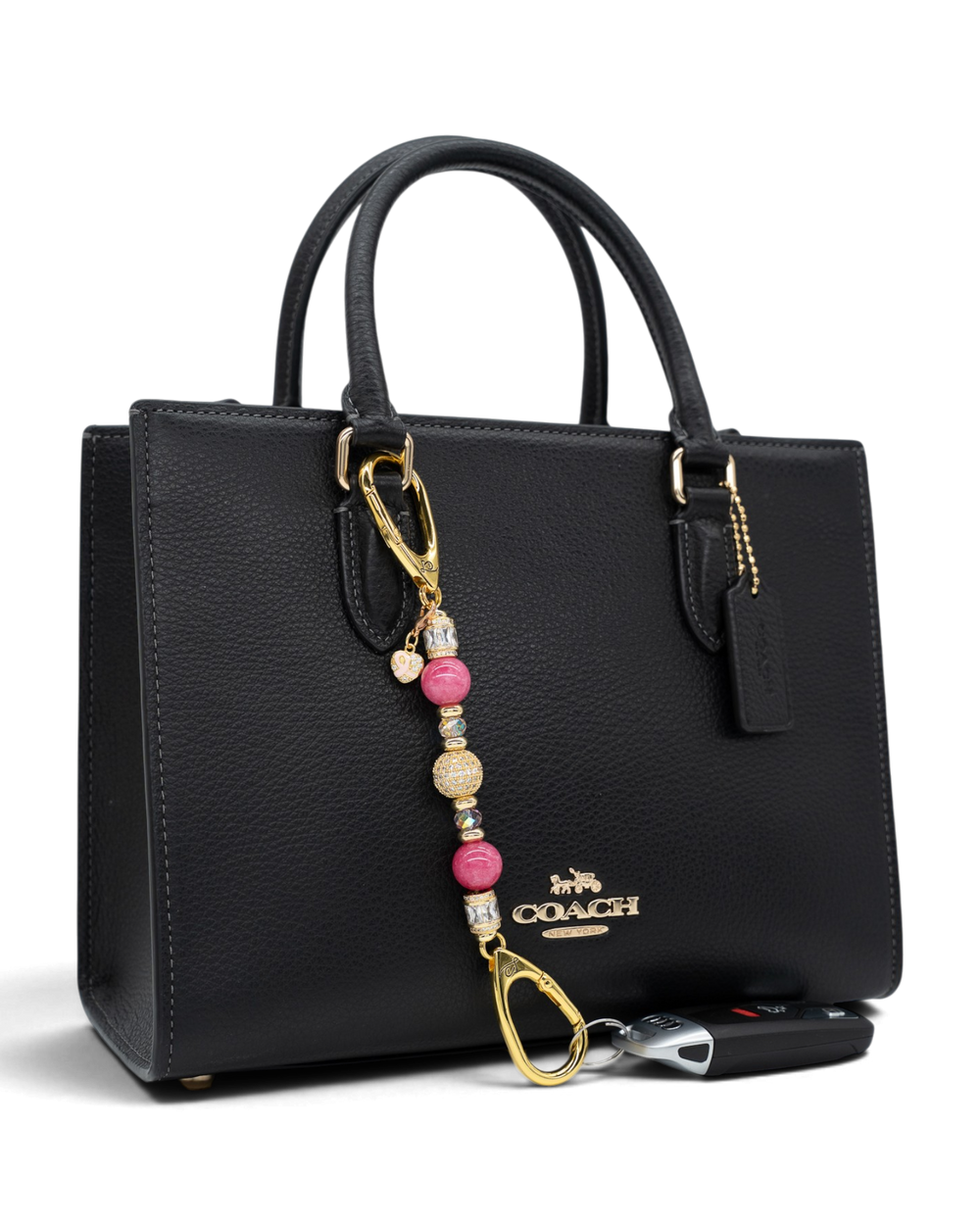 LD Keyfinder Petite Radiant Hope beaded charm with pink jade and gold accents attached to a black leather handbag.