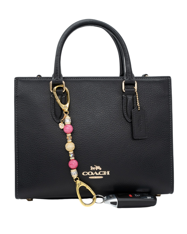 LD Keyfinder Petite Radiant Hope accessory with pink jade and gold charms attached to a black leather handbag.