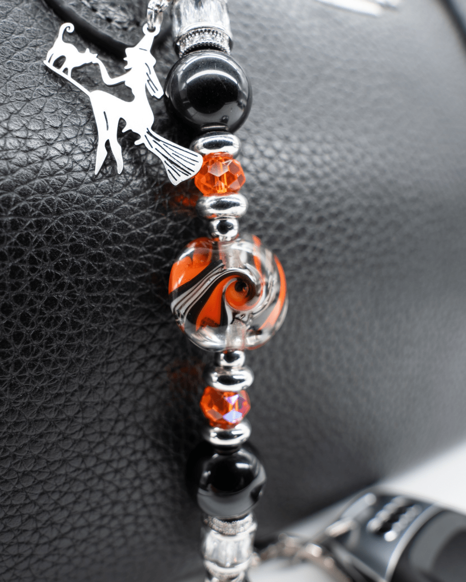 LD Keyfinder Petite Spellbound accessory with black obsidian, orange glass, and a witch charm on a black leather bag.