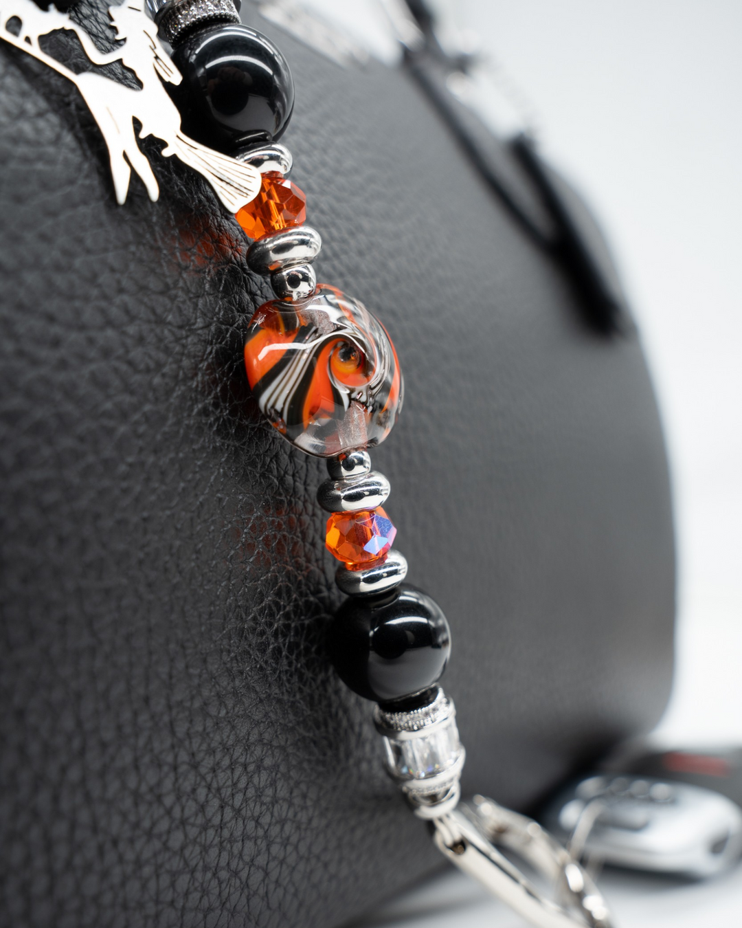 LD Keyfinder Petite Spellbound accessory with black obsidian, orange glass beads, and a witch charm on a black bag.