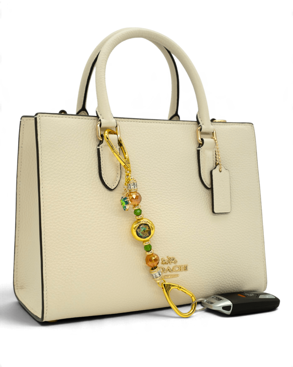 LD Keyfinder Petite Verdant Flame accessory with orange and green glass beads and gold leaf charm on a cream handbag.