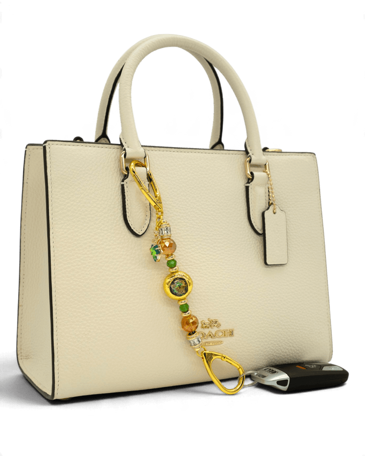 LD Keyfinder Petite Verdant Flame accessory with orange and green glass beads and gold leaf charm on a cream handbag.