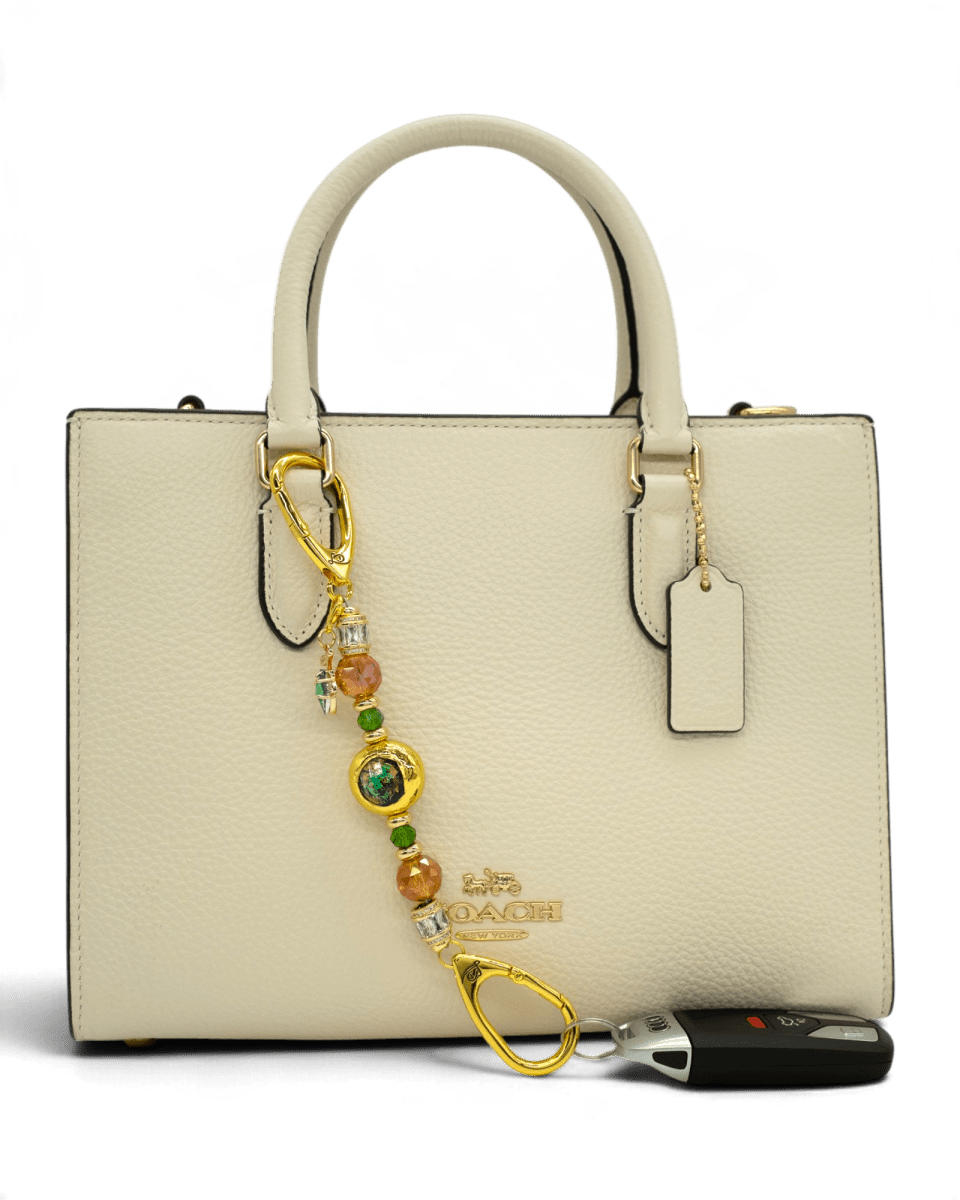 LD Keyfinder Petite Verdant Flame accessory with orange and green glass beads and gold leaf charm on a cream handbag