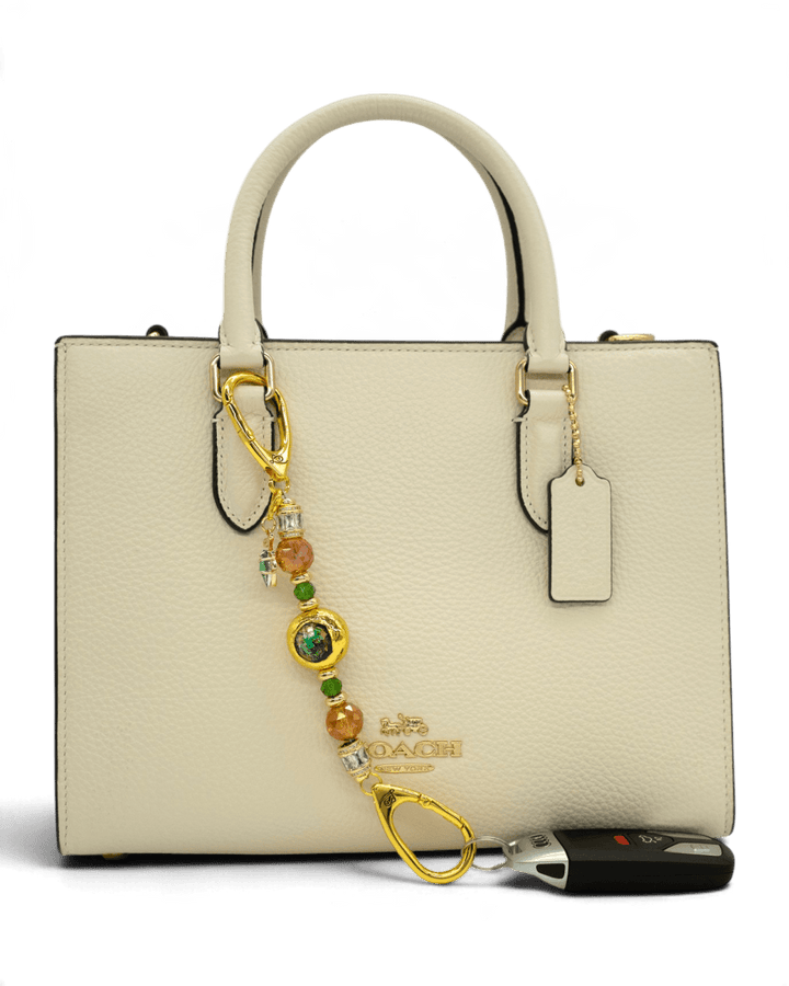 LD Keyfinder Petite Verdant Flame accessory with orange and green glass beads and gold leaf charm on a cream handbag