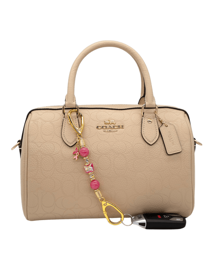 LD Keyfinder Wings of Hope Mini beaded keychain with pink jade and butterfly charm attached to a beige Coach handbag