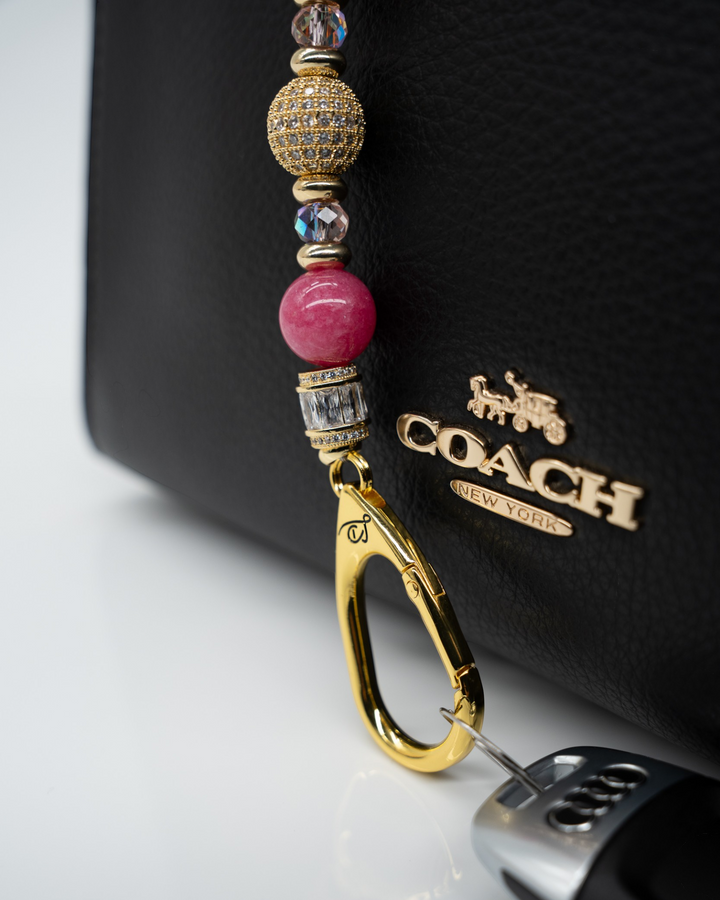 LD Keyfinder Petite Radiant Hope beaded accessory with pink jade and gold rhinestones attached to a black leather bag.