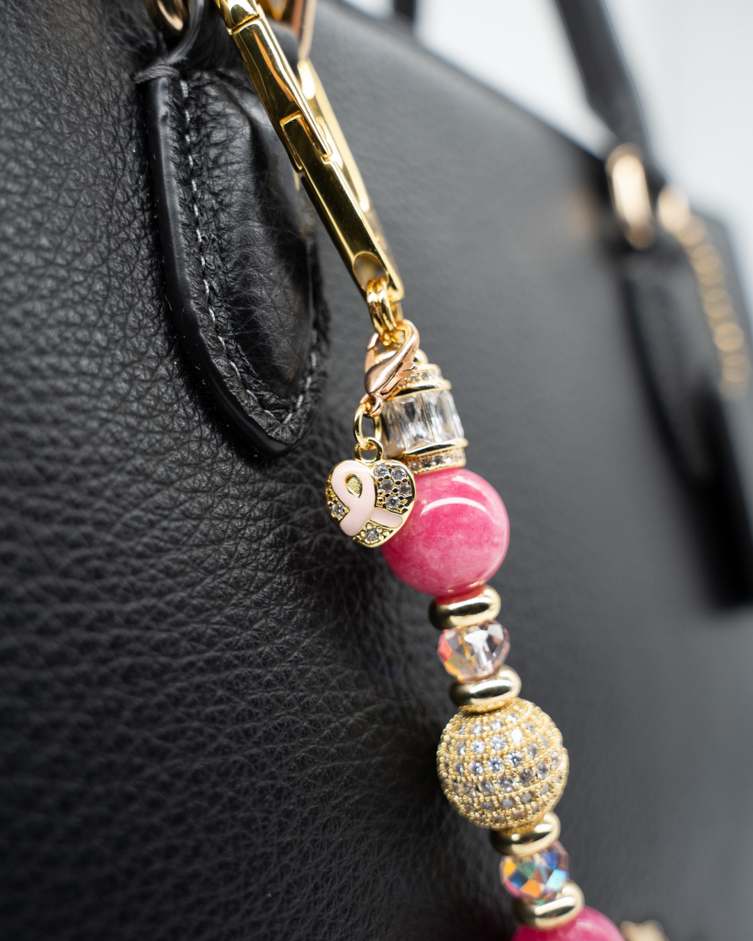 LD Keyfinder Petite Radiant Hope charm with pink jade beads, gold pavé centerpiece, and pink ribbon heart on a bag.
