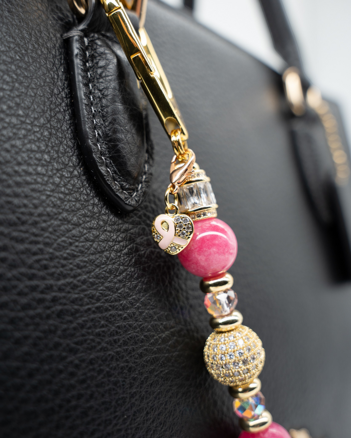 LD Keyfinder Petite Radiant Hope charm with pink jade beads, gold pavé centerpiece, and pink ribbon heart on a bag.