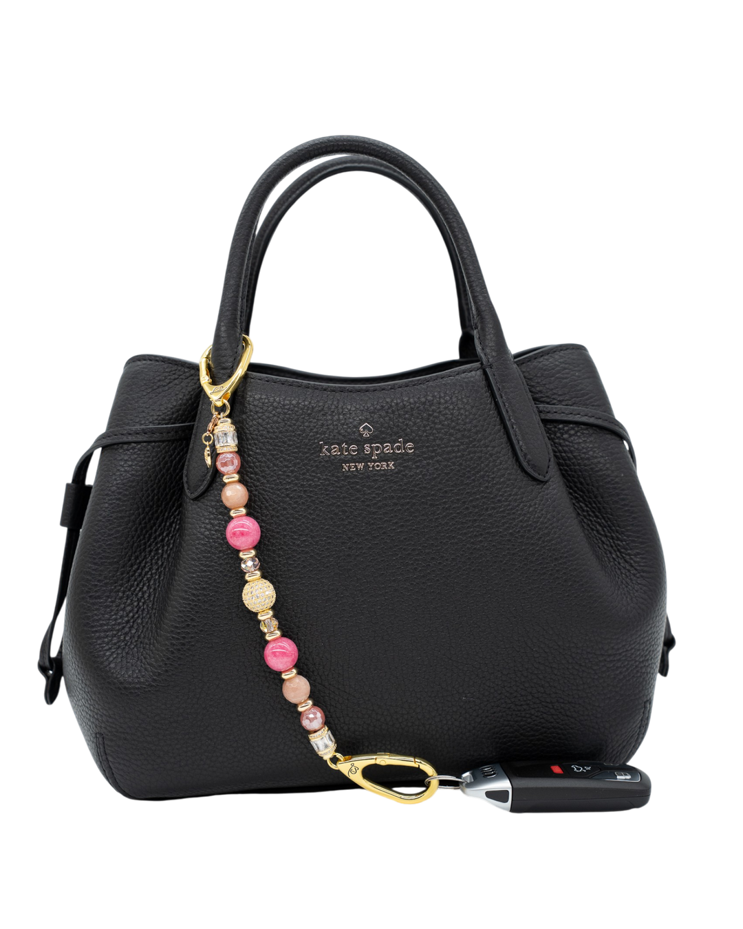 LD Keyfinder Radiant Hope beaded keychain with pink gemstones and gold ribbon charm attached to a black leather handbag