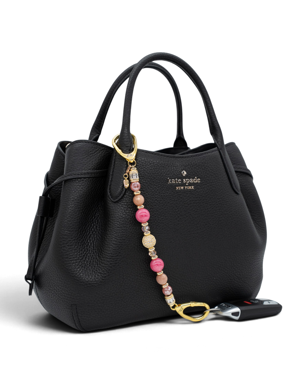 LD Keyfinder Radiant Hope beaded keychain with pink gemstones and gold ribbon charm attached to a black leather handbag.