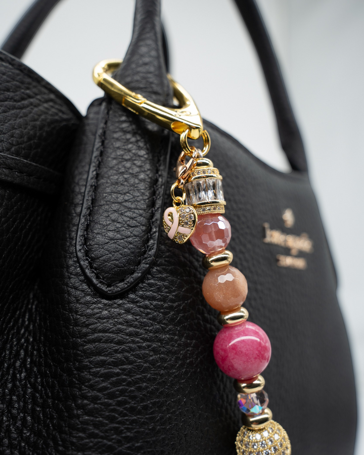 LD Keyfinder Radiant Hope breast cancer awareness charm with pink gemstones, gold accents, and a ribbon heart on a bag