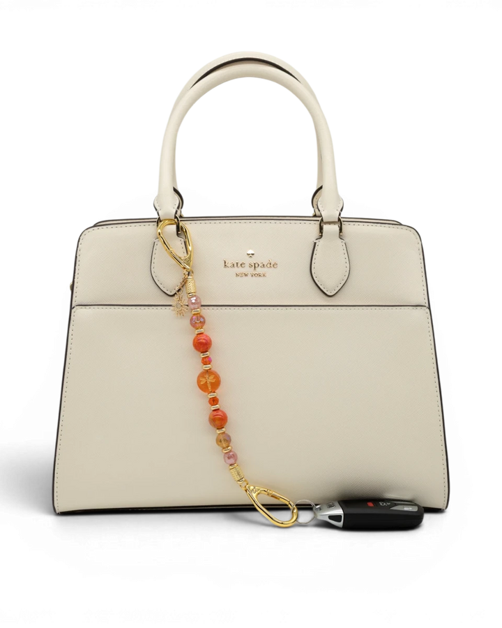 LD Keyfinder Summer Sunset beaded accessory with cherry quartz, agate, and dragonfly charm attached to a white handbag.