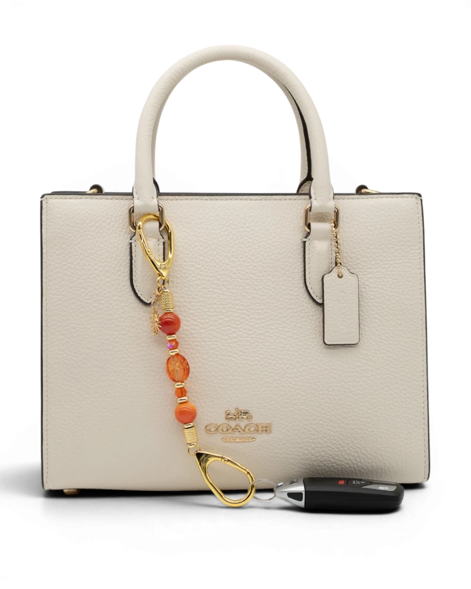LD Keyfinder Summer Sunset Mini beaded accessory with coral glass, agate, and gold sun charm on a white handbag.