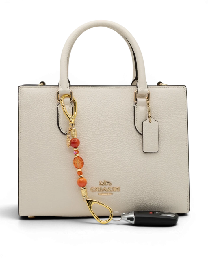 LD Keyfinder Summer Sunset Mini beaded accessory with coral glass, agate, and gold sun charm on a white handbag.