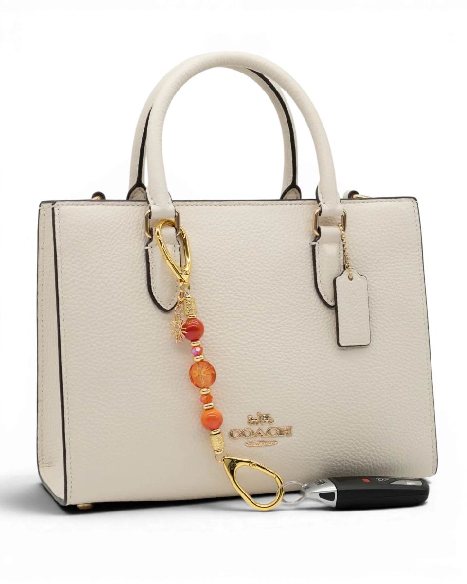 LD Keyfinder Summer Sunset Mini beaded accessory with coral glass, agate beads, and gold sun charm on a white handbag.
