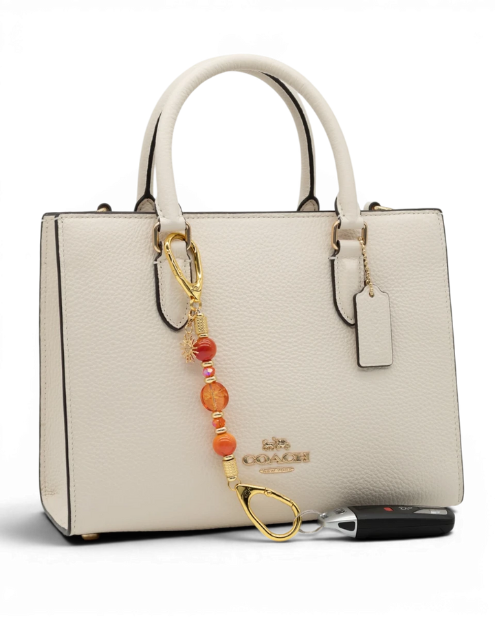 LD Keyfinder Summer Sunset Mini beaded accessory with coral glass, agate beads, and gold sun charm on a white handbag.