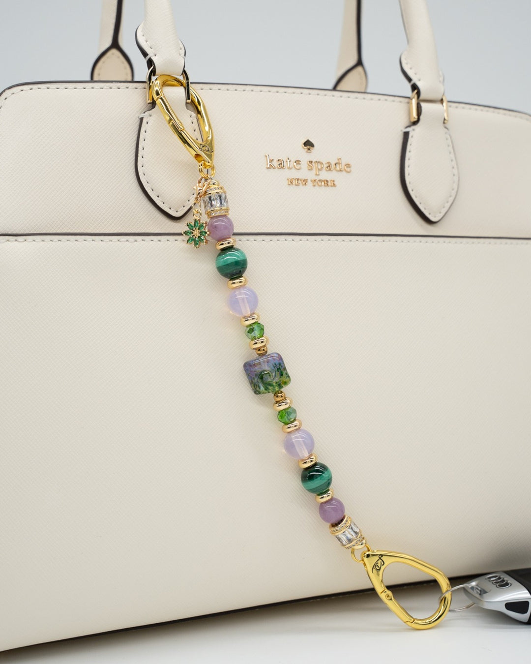 LD Keyfinder Verdant Bloom beaded accessory with malachite, lepidolite, and lampwork glass attached to a cream handbag.
