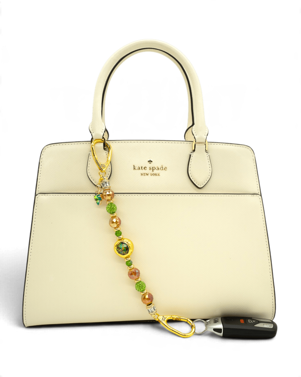 LD Keyfinder Verdant Flame accessory with green and orange beads and gold charm attached to a cream handbag.