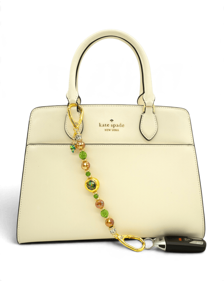 LD Keyfinder Verdant Flame accessory with green and orange beads and gold charm attached to a cream handbag.