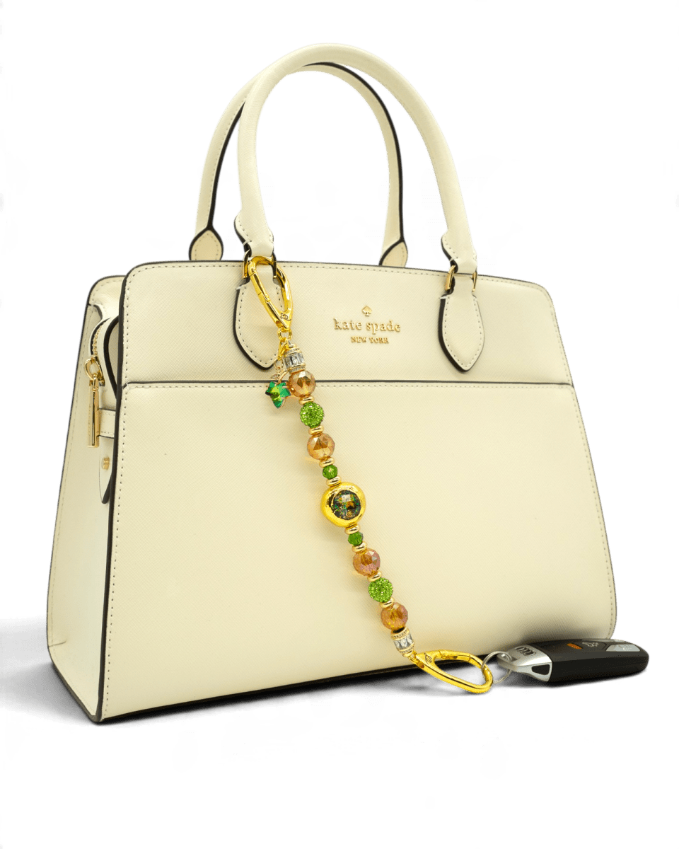 LD Keyfinder Verdant Flame beaded accessory with green and orange crystals and gold accents hanging on a cream handbag
