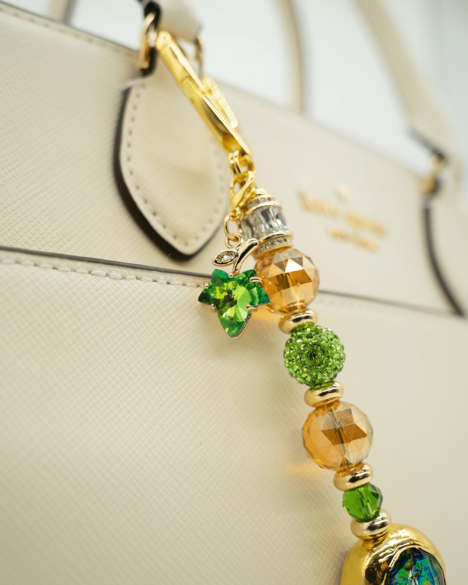 LD Keyfinder Verdant Flame bag charm with green and orange beads, gold accents, and a green glass leaf charm on a bag