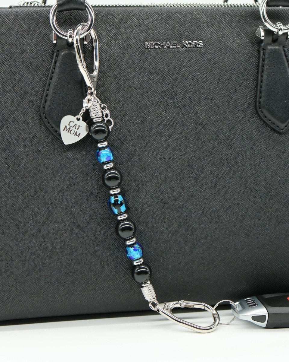 LD Keyfinder Whisker Dreams beaded keychain with black obsidian, blue lampwork glass, and Cat Mom charm on a handbag.