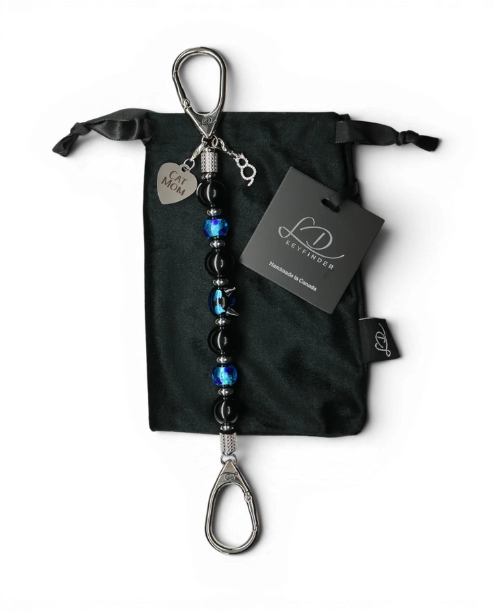 LD Keyfinder Whisker Dreams beaded keychain with black obsidian, blue foil glass, and Cat Mom charm on velvet bag