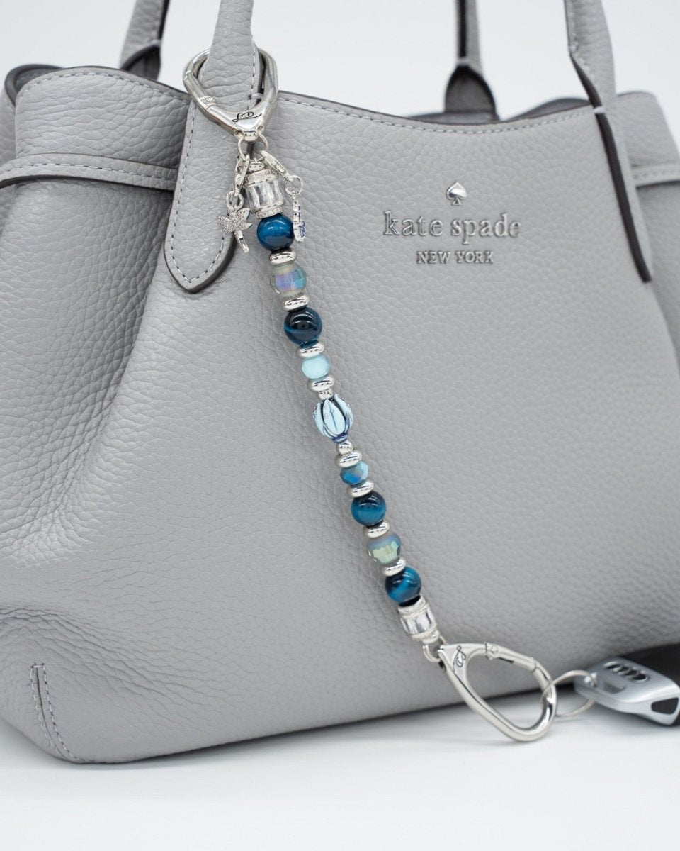 LD Keyfinder Whispering Garden featuring blue tiger eye, glass beads, and charms attached to a grey leather handbag