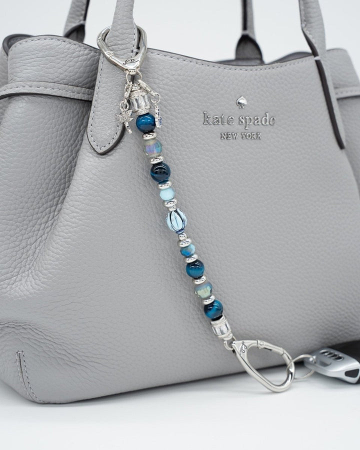 LD Keyfinder Whispering Garden featuring blue tiger eye, glass beads, and charms attached to a grey leather handbag