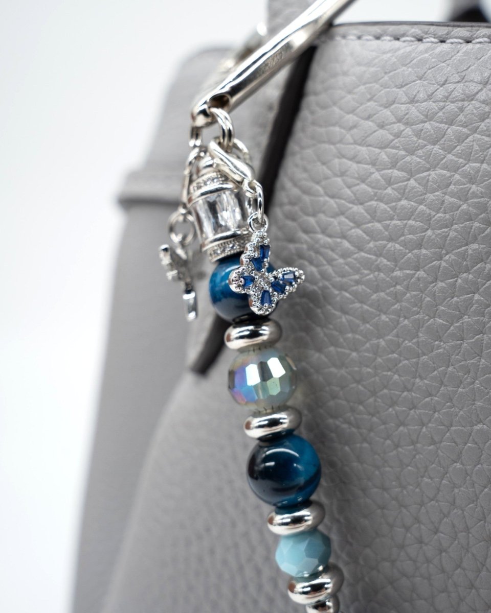 LD Keyfinder Whispering Garden accessory with blue tiger eye, glass beads, and a rhinestone butterfly charm on a bag.