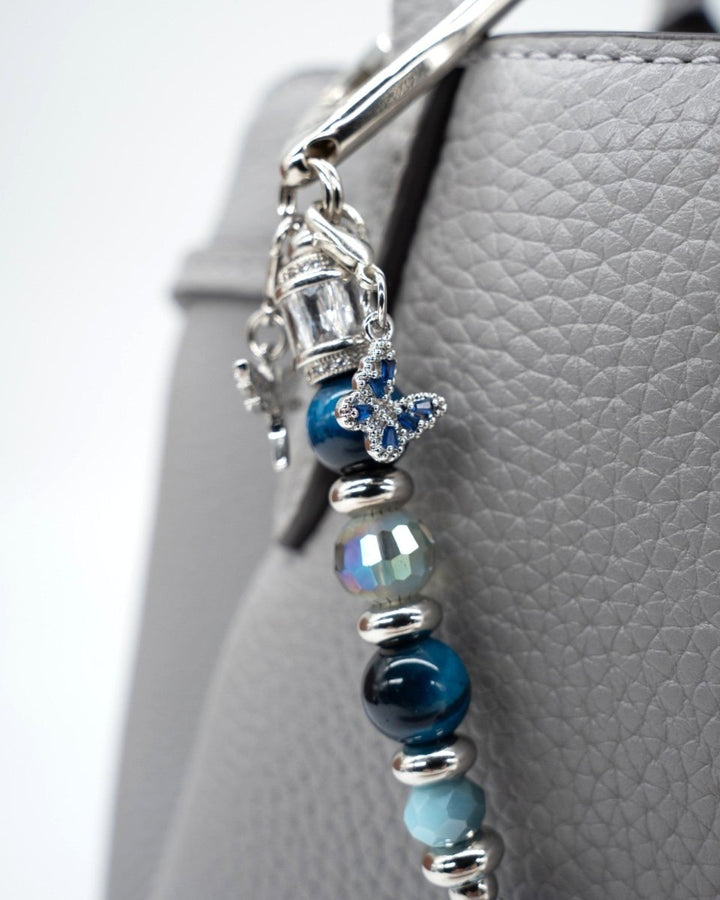 LD Keyfinder Whispering Garden accessory with blue tiger eye, glass beads, and a rhinestone butterfly charm on a bag.