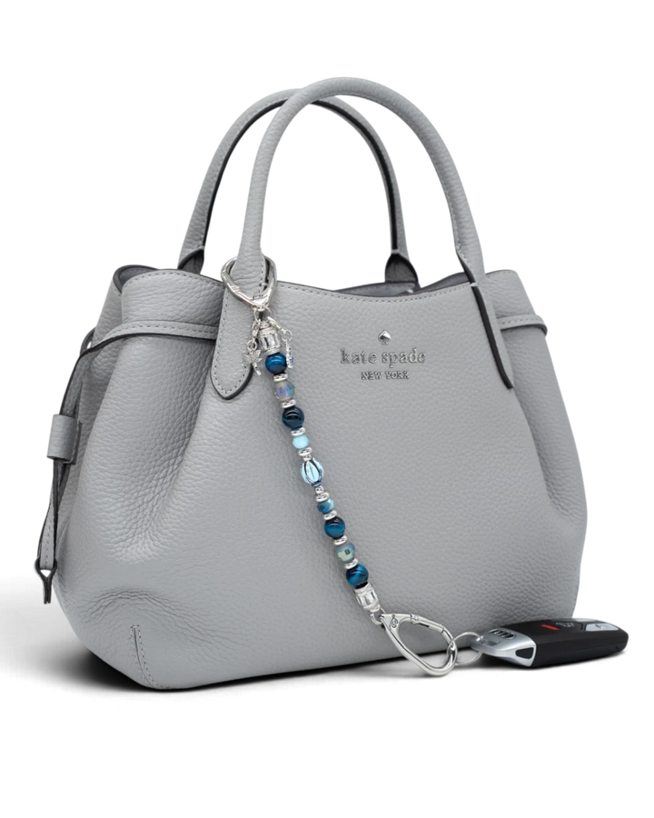 LD Keyfinder Whispering Garden beaded keychain with blue glass tulip, tiger eye, and charms attached to a grey handbag